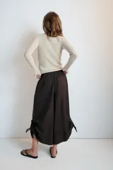 Pantalón culotte de tiro medio, color verde militar, con cintura elástica y bolsillos laterales ocultos. Presenta un diseño de bajo ancho con aberturas ajustables mediante cordones fruncidos en los laterales.