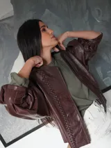 Campera de cuero con silueta oversize y corte levemente corto. Presenta cierre frontal metálico, cuello a la base y mangas amplias con detalles trenzados y recortes que aportan textura.