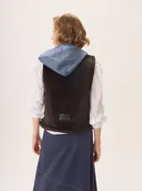 Chaleco con capucha, presenta una espalda de pelo sintético en color marrón oscuro con etiqueta de cuero negra y una capucha de tela tipo denim azul. Diseño original con mezcla de texturas.