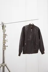 Campera tipo bomber de cuero ovino color marrón oscuro, con cuello de tejido acanalado y cierre frontal con cremallera.