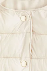 Campera acolchada de nylon color beige, con cuello redondo, cierre de botones a presión y bolsillos laterales discretos. Tiene elástico fino en los puños y está forrada.