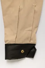 Bombacha de campo de gabardina color beige, de corte holgado con costuras verticales decorativas y botamangas negras abotonadas.