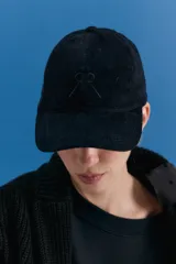 Gorra tipo cap confeccionada en corderoy negro, con isologo bordado en el frente y tira de ajuste con hebilla metálica en la parte posterior.