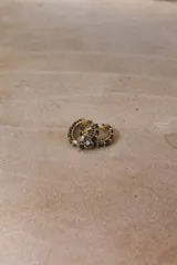 Aros tipo argolla pequeña de base metálica dorada con incrustaciones de cristales transparentes en la parte frontal.