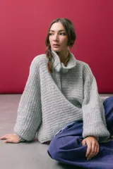 Buzo tejido en mohair de color gris, con silueta amplia y corte en línea A. Presenta cuello tipo remera con broches que permiten cerrarlo como polera, mangas largas con puños y un diseño de tejido horizontal.
