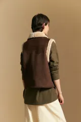 Chaleco negro de gamuza sintética con interior y bordes de corderito sintético. Presenta un diseño sin mangas con cuello solapa y cierre frontal.
