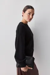 Sweater negro de tejido suave con escote redondo, mangas largas y calce relajado, con terminaciones acanaladas en cuello, puños y ruedo.