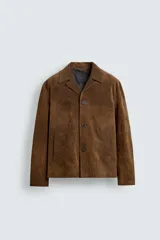 Sobrecamisa de corte relajado confeccionada en piel con acabado de ante. Presenta cuello tipo bowling, cierre frontal con botones, manga larga con puños abotonados y bolsillos de vivo en la parte frontal.