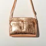 Bandolera rectangular color rosa metalizado, con correa larga regulable y cierre con broche a presión.