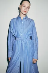 Vestido midi de corte camisero con estampado de rayas verticales, cuello solapa, manga larga con puños y cierre frontal con botones. Incluye un cinturón de lazada en el mismo tejido y bolsillos laterales ocultos.