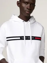 Buzo con capucha y cordón ajustable Tommy Hilfiger, color blanco, de corte regular. Presenta un bolsillo estilo canguro en la parte delantera y una franja horizontal en el pecho con el logotipo y los colores distintivos de la marca.