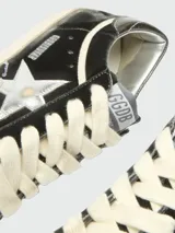 Zapatillas Golden Goose modelo Super Star, confeccionadas en terciopelo negro con acabado desgastado. Presentan la icónica estrella lateral en cuero plateado, cordones gruesos en color crema y suela de goma con efecto envejecido.