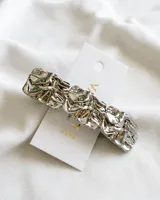 Broche plateado para el pelo con diseño texturizado.