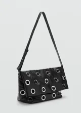 Bolso tipo tote de color negro, confeccionado en poliuretano, con diseño de ojales metálicos plateados distribuidos por toda la superficie y asas largas para llevar al hombro.