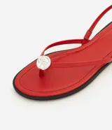 Sandalias planas rojas con diseño de dedo, tiras finas y aplique metalizado decorativo.