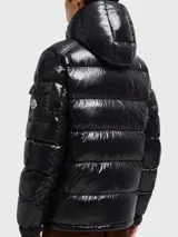 Campera puffer corta de Moncler, modelo Maya, con acabado brillante, capucha desmontable y cierre frontal con cremallera. Presenta bolsillos laterales y un bolsillo con solapa en la manga izquierda.