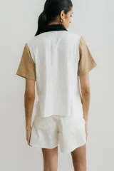 Camisa de manga corta con diseño color block, combinando paneles blancos, verde oliva y detalles en negro (cuello, tapeta de botones y bolsillos de parche).