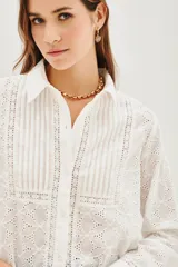 Camisa de manga larga en color blanco, confeccionada en tejido de algodón con diseño calado tipo broderie. Presenta cuello clásico, cierre frontal con botones y paneles frontales con tablas verticales.