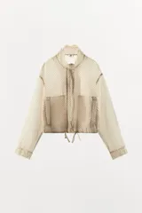 Chaqueta ligera de cuello subido y manga larga con estampado de lunares. Cuenta con bolsillos frontales de vivo, cierre de cremallera y botones a presión ocultos por solapa, y cordones ajustables en el bajo.