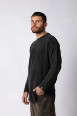 Sweater de punto grueso color negro con efecto gastado, cuello redondo, mangas largas y detalles de roturas en puños y ruedo. Presenta un diseño con letras bordadas al tono en el frente.