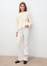 Chaqueta de tweed color crema con cuello redondo, cierre frontal con botones y dos bolsillos de parche delanteros. Presenta terminaciones deshilachadas y forro interior.