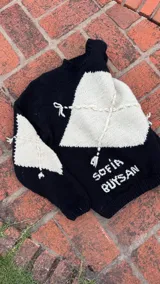 Buzo tejido a mano con diseño de rombos en contraste blanco y negro, cuello redondo y mangas largas.