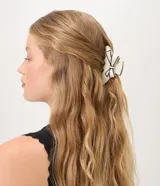 Pinza de pelo tipo clip, color crema con bordes negros contrastantes y detalle de lazo decorativo aplicado en la parte superior.