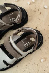 Sandalias de cuero marrón con diseño de tiras anchas y ajuste mediante velcro. Presentan una plantilla acolchada color tostado con detalles en rojo y una suela de goma negra con plataforma dentada.