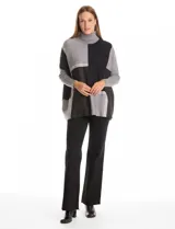 Polera tipo poncho de corte oversize, con cuello alto tejido y mangas largas con puños elásticos. Presenta un diseño geométrico de bloques de color en tonos beige, gris y tostado.