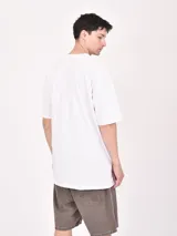 Remera blanca de corte oversized con estampado frontal de letras en color naranja y negro.