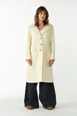 Tapado largo color crema de lana fina sin teñir, con cuello con solapa, manga larga, forrado, con bolsillos y cierre frontal con botones.