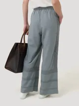 Pantalón de corte amplio y tiro alto, confeccionado en una mezcla de lino orgánico y viscosa. Presenta cintura elástica con cordón ajustable y detalles de encaje broderie tono sobre tono en los laterales y en el ruedo.