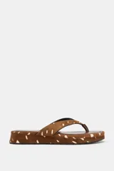 Sandalia plana tipo ojota con plataforma baja, confeccionada en piel con estampado animal print tipo ciervo en tonos marrones y blancos. Tiras separadoras de dedos forradas en el mismo material y suela con base dentada.