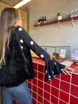 Blusa negra con estampado de lunares blancos, de corte ajustado al cuerpo, cuello redondo y mangas largas con terminación acampanada.