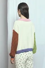 Cardigan de punto color marrón, con cuello vuelto, cierre frontal de botones y detalles de ribetes a rayas en los puños, la cintura y la botonera. Las mangas presentan un diseño tejido en relieve con textura de ochos.