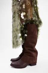 Bota de caña alta confeccionada en cuero vacuno, con diseño de solapa superior y taco bajo cuadrado.