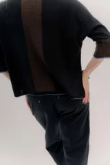 Buzo de punto en color negro con mangas tres cuartos y puños en contraste color marrón. Presenta un diseño holgado con tajos laterales y un aplique circular con logo en la parte inferior.