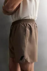 Pantalón corto deportivo color marrón oliva, confeccionado en tejido técnico ligero y elástico, con forro interior. Presenta cintura elástica ajustable con cordón, bolsillos frontales, bolsillo de seguridad trasero con cierre y aberturas laterales en el bajo.