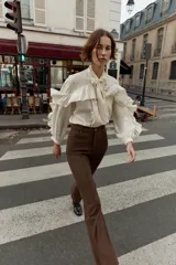 Pantalón de tiro alto color marrón oscuro, con corte flare (campana) y nervio marcado en el frente de ambas piernas. Presenta bolsillos delanteros y bolsillos de plastrón en la espalda.