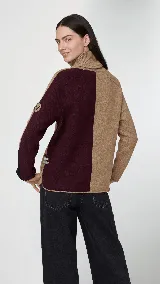 Polera de cuello alto confeccionada en lana lambswool, con diseño bicolor en negro y marrón. Presenta mangas largas con franjas verticales en gris y un parche circular bordado en la manga derecha.