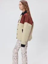 Campera acolchada de diseño colorblock, con el pecho y hombros en tono bordó y el cuerpo y mangas en color beige. Presenta cuello camisero y puños de pana negra, cierre frontal oculto con botones a presión y costuras pespuntadas en patrón cuadriculado.