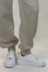 Pantalon deportivo tipo babucha de color beige, con cintura elástica ajustable mediante cordón y puños elásticos en los tobillos.