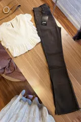 Jeans de corte flare color marrón oscuro, confeccionados en denim, con tiro medio, bolsillos clásicos y detalle de dobladillo deshilachado con pequeña abertura lateral en los tobillos.