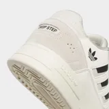 Championes Adidas Drop Step Low 2.0 de estilo urbano, con diseño inspirado en el baloncesto. Presentan una parte superior que combina ante y piel sintética en tonos crema y blanco, con las icónicas tres tiras laterales en color negro y el logo del trébol. Cuentan con una suela de goma esculpida y cierre de cordones.