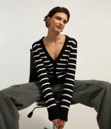Cardigan corto de punto con diseño listrado en blanco y negro, escote en V, cierre frontal con botones y manga larga.