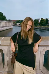 Camiseta negra de algodón con cuello redondo, manga corta y detalle de aplicación de encaje a tono en los puños. Presenta un diseño con bajo asimétrico y frunce lateral.