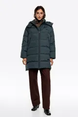 Campera tipo puffer de largo medio con silueta en línea A, confeccionada en tejido técnico. Presenta cierre frontal con cremallera, cuello subido con capucha desmontable y mangas largas con puño interior elástico. Incorpora bolsillos con cremallera, aberturas laterales ajustables y logo bordado en el pecho.