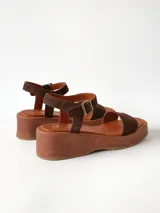 Sandalias de plataforma color chocolate con tira frontal ancha de gamuza y tira al tobillo con hebilla metálica ajustable.