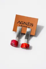 Aros colgantes compuestos por una pieza rectangular metálica plateada y un dije inferior de piedra roja resinosa con detalle cúbico metálico.