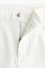 Short de denim de algodón rígido, color blanco, de tiro alto con cinco bolsillos, cierre de cremallera con botón y terminación deshilachada en el bajo.